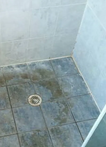 A shower floor before regrouting: stained, failing grout