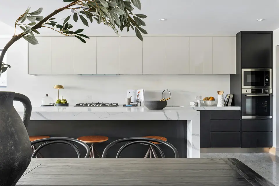 A modern kitchen with a marble waterfall island and dark cabinetry