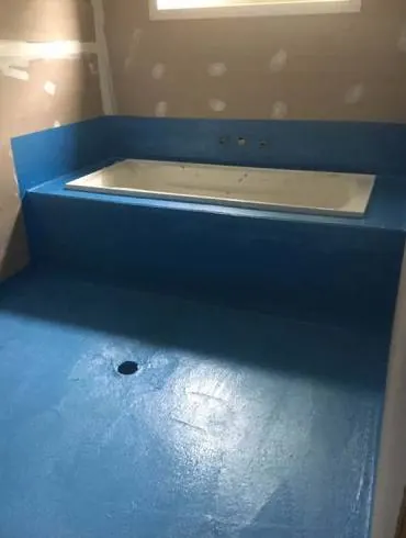 Blue waterproofing membrane across a bathroom floor and bath surround