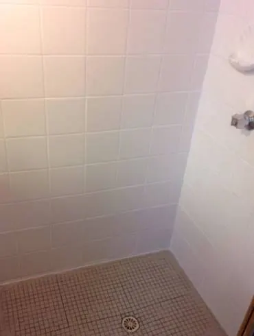 A white-tiled shower recess with a mosaic floor