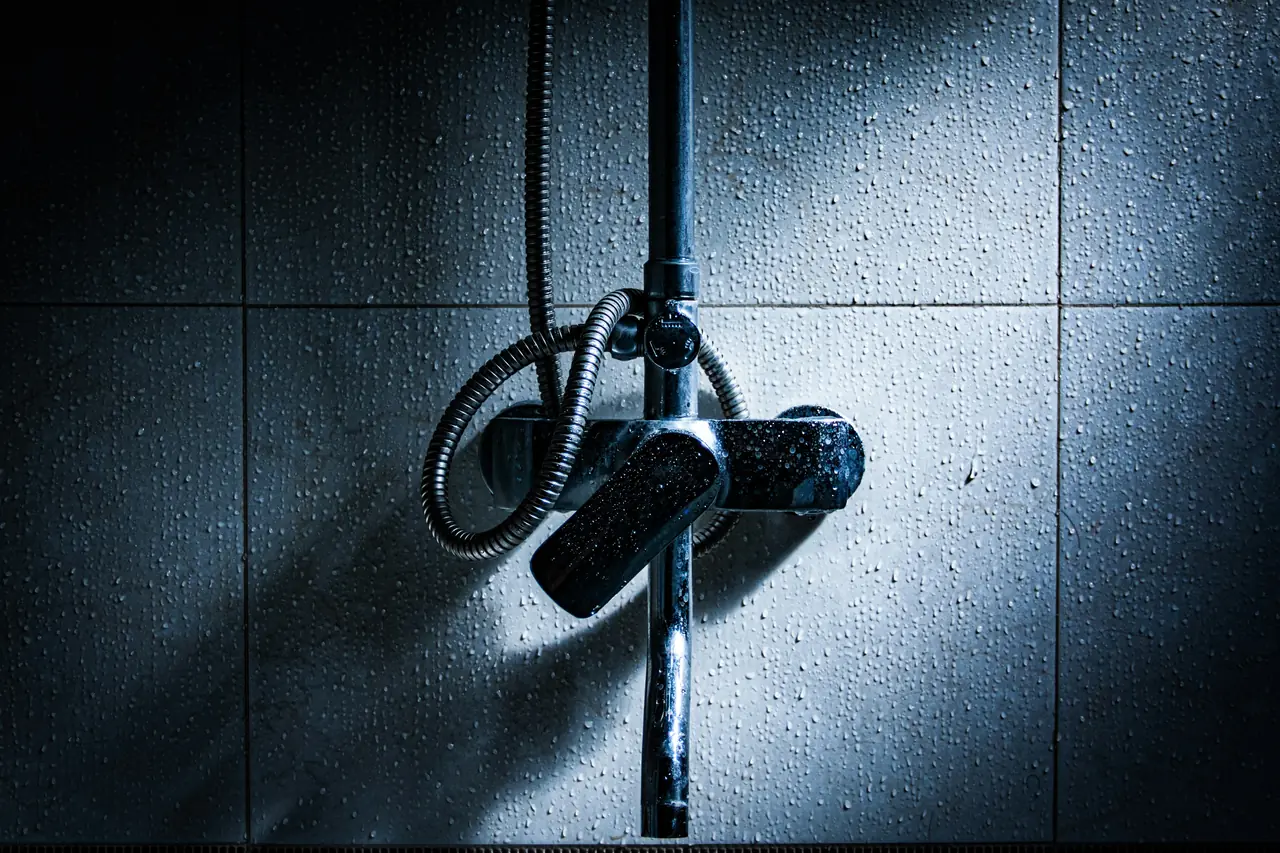 A chrome shower mixer on wet, tiled walls